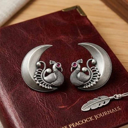 Traditional peacock moon earrings displayed on leather journal