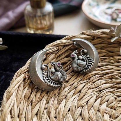 Antique silver peacock moon earrings styled on wicker basket