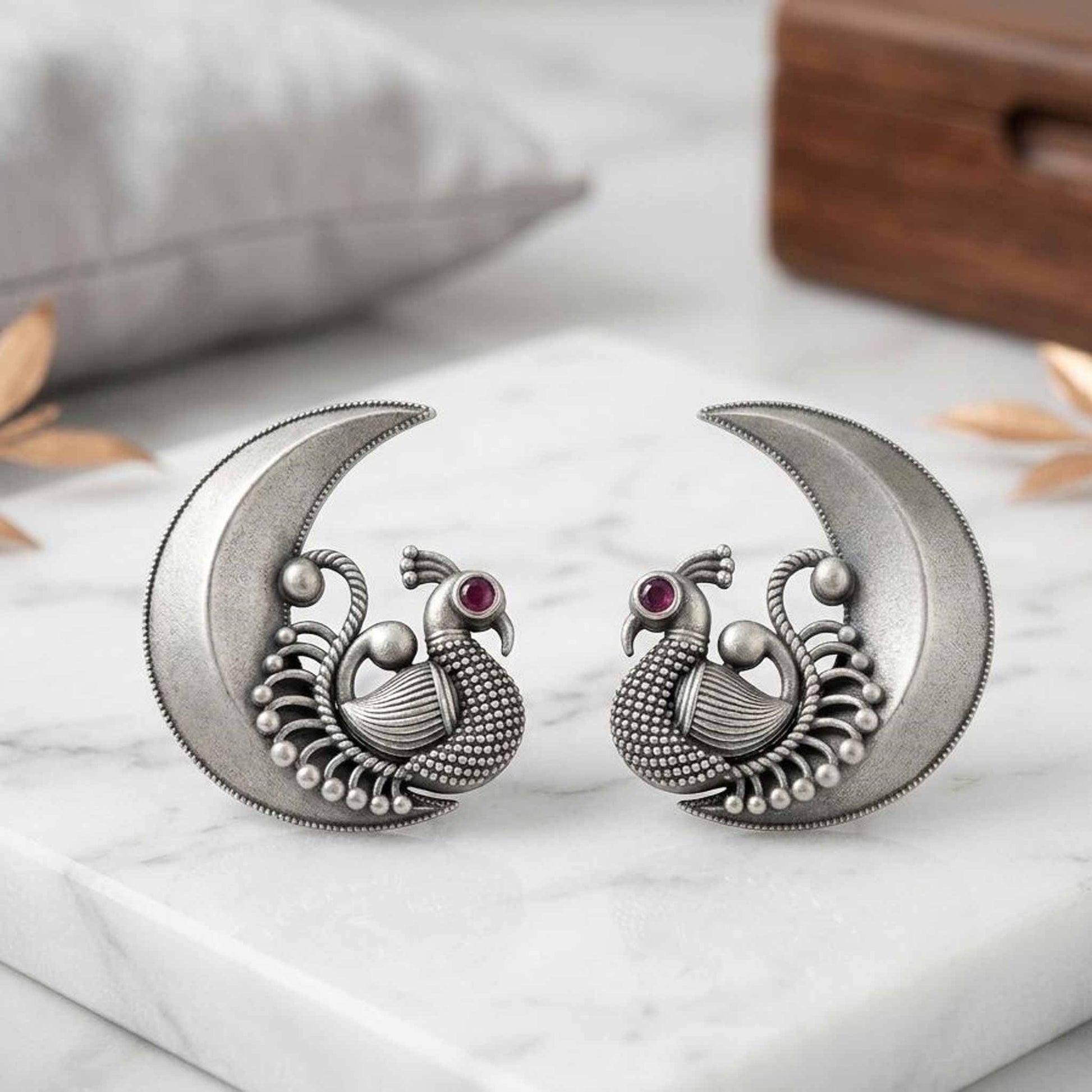 Peacock moon stud earrings displayed on marble platform