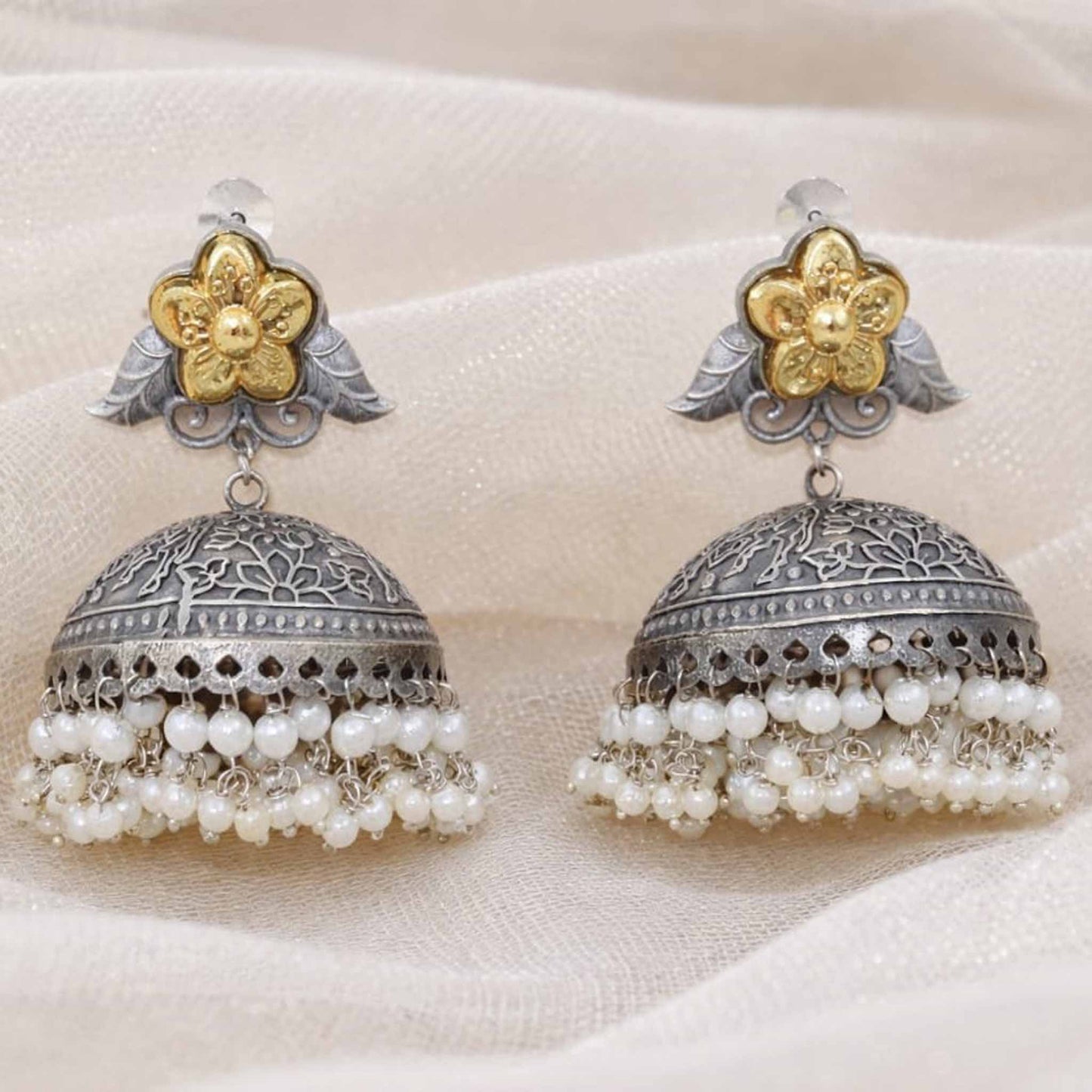 Closeup of floral pearl jhumka earrings on fabric backdrop