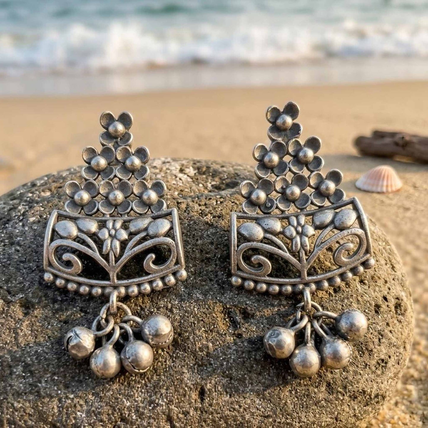 Floral ghungroo German Silver earrings displayed on beach rock