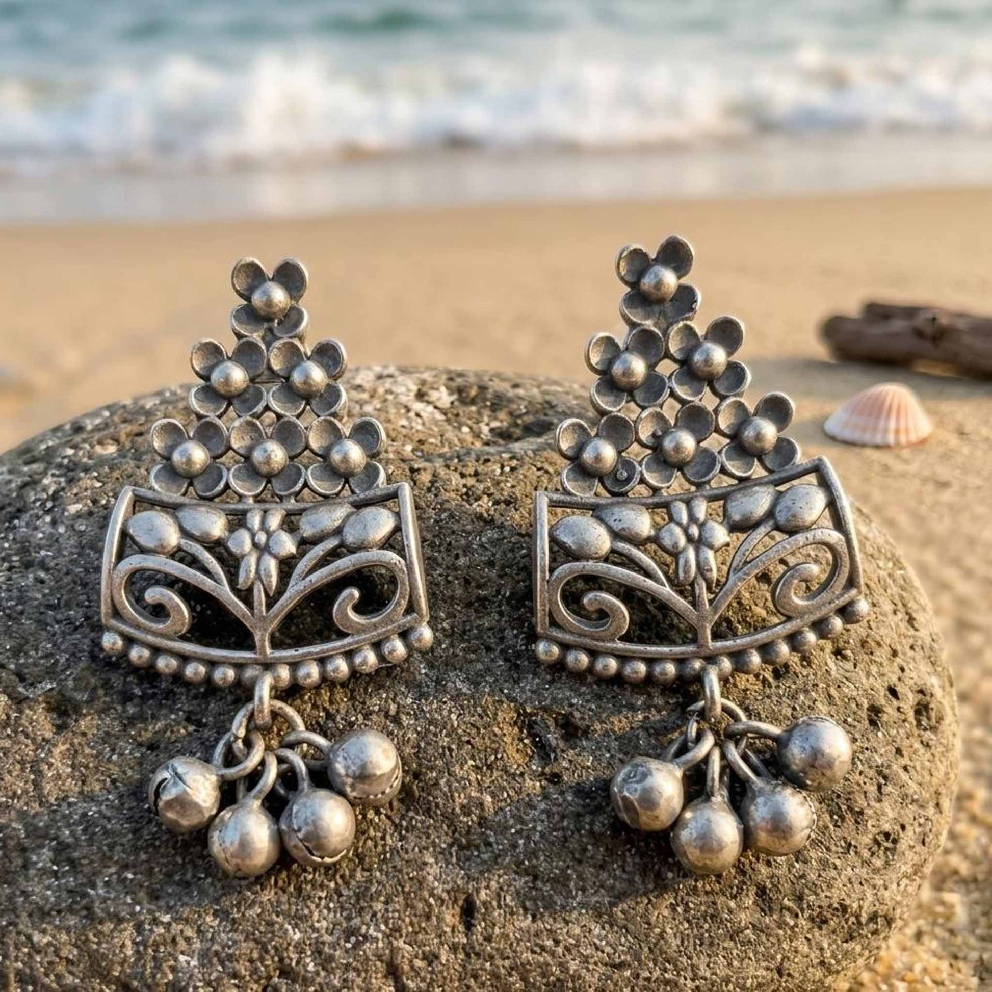 Floral ghungroo German Silver earrings displayed on beach rock
