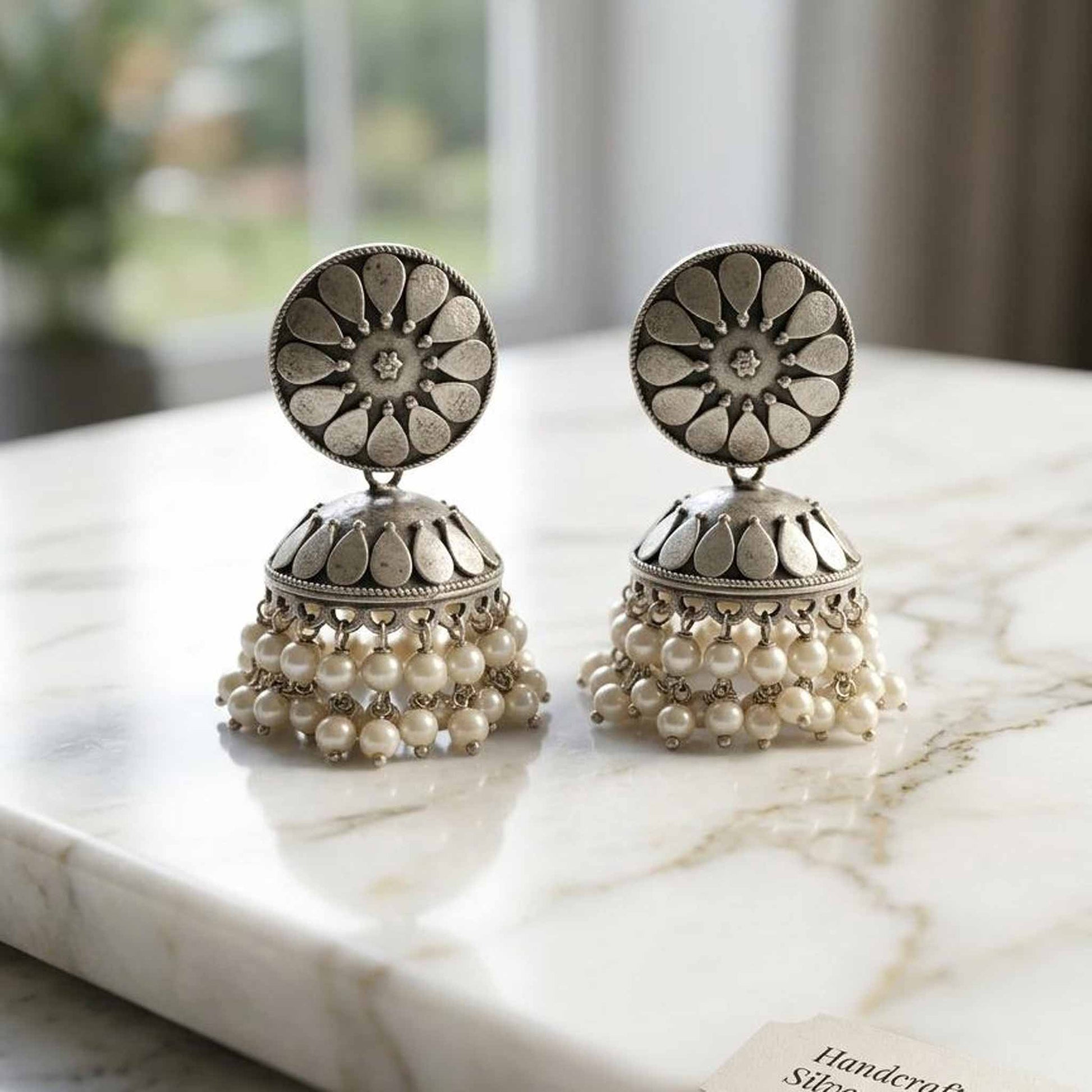 German silver pearl jhumka earrings on marble surface