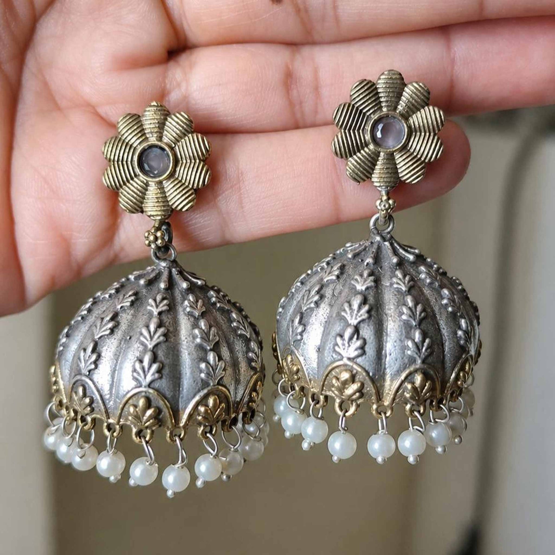 Hand holding embossed pearl jhumka earrings