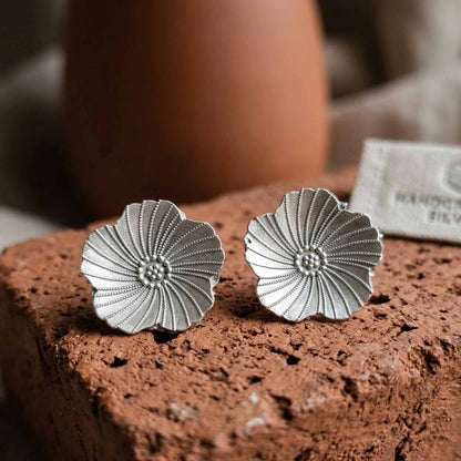 Minimal silver floral earrings styled on textured surface