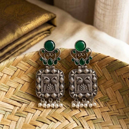 Handcrafted emerald German silver earrings on woven tray