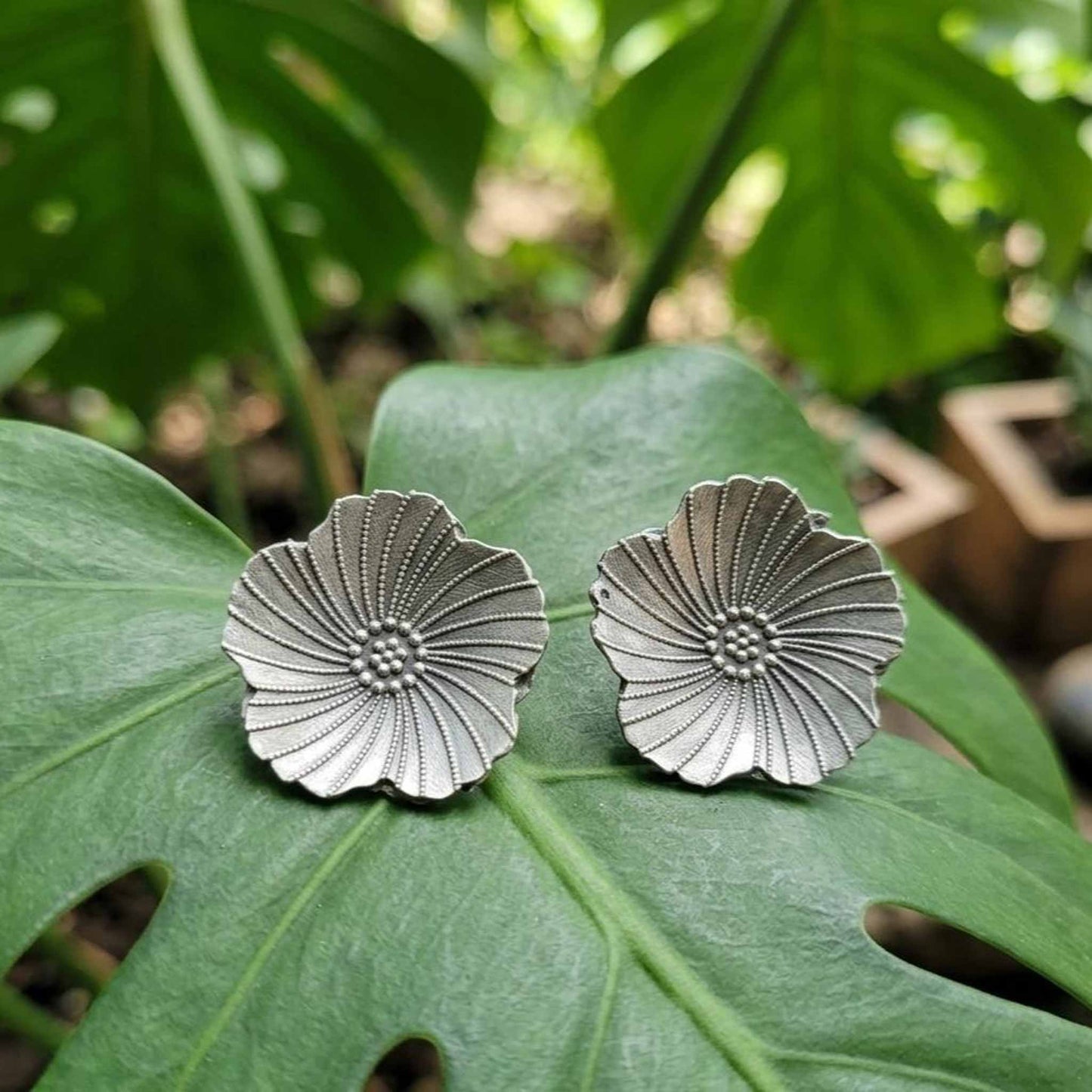 Silver floral stud earrings on tropical leaf background