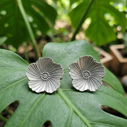 Silver floral stud earrings on tropical leaf background