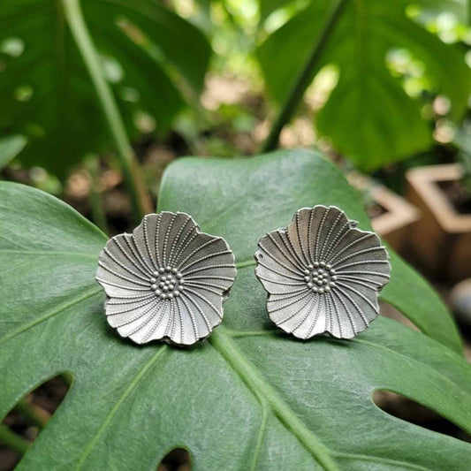 Silver floral stud earrings on tropical leaf background