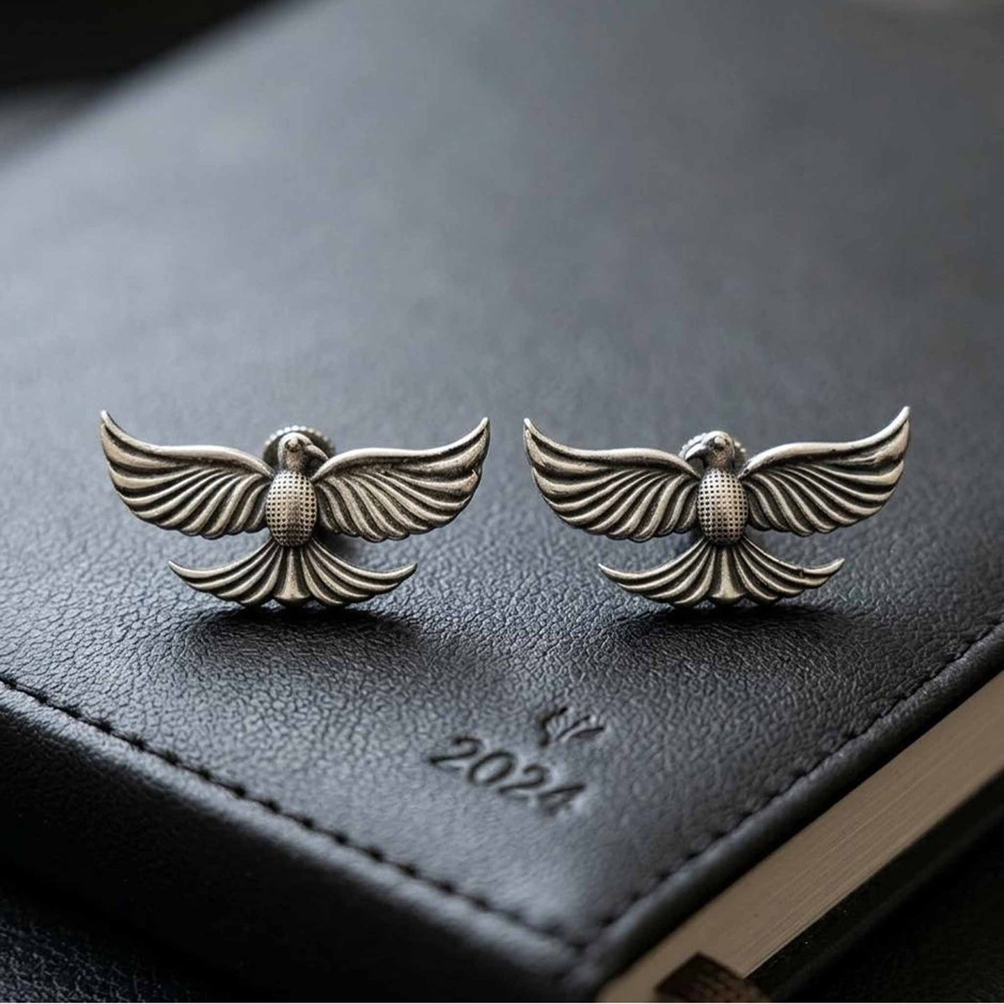 Antique silver bird motif earrings on black textured surface