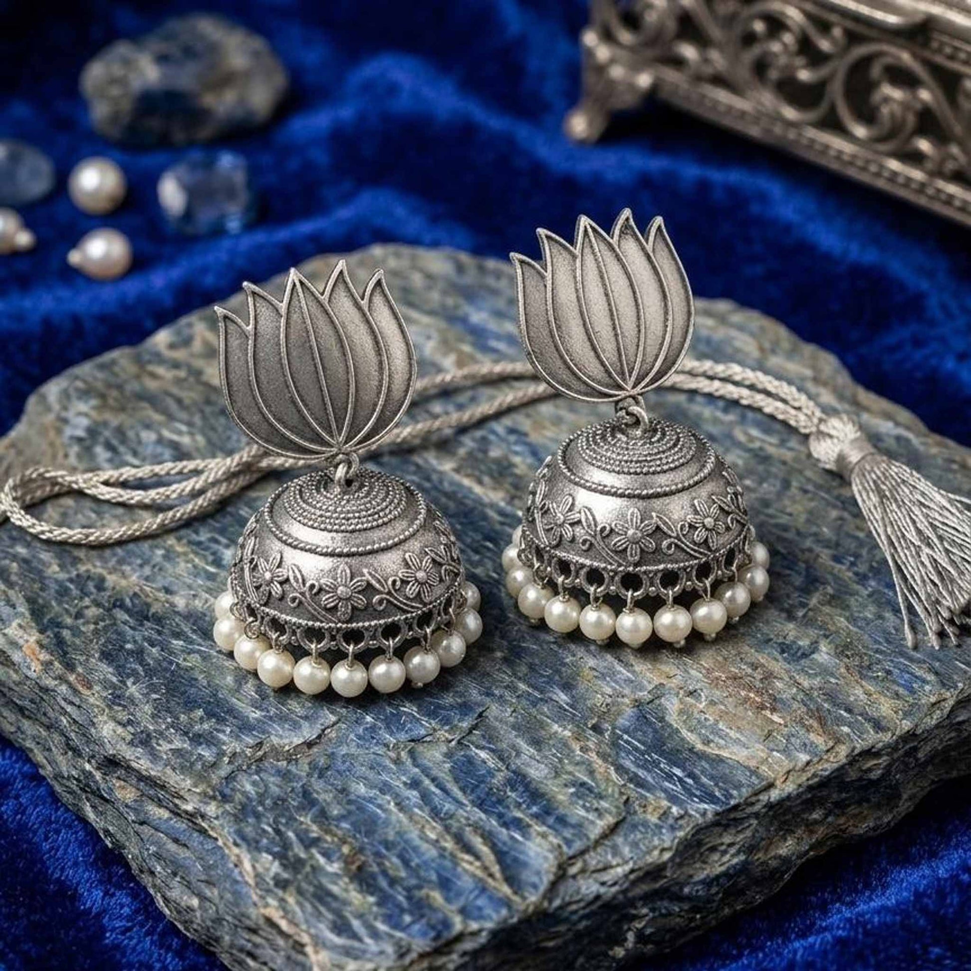 Handcrafted lotus pearl jhumka earrings on blue stone background