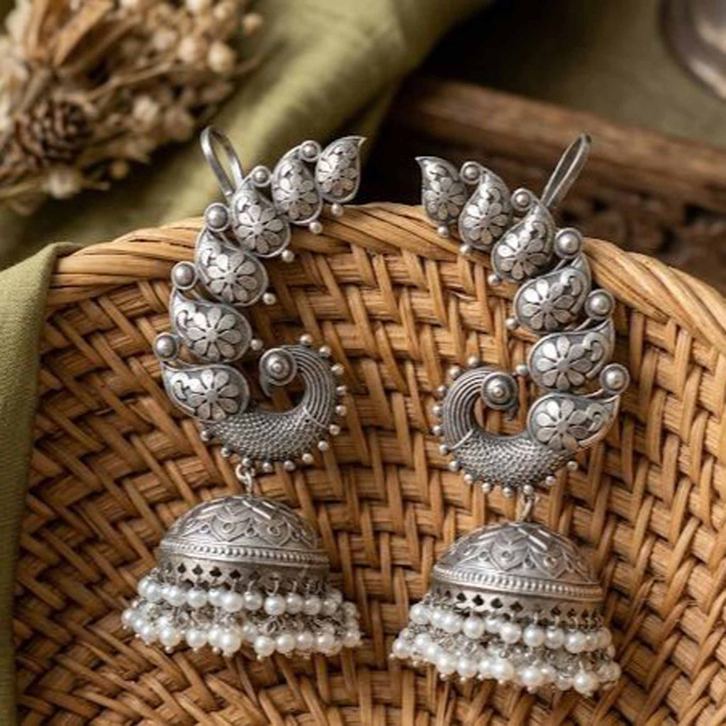 Peacock earcuff pearl jhumka earrings displayed on wicker basket