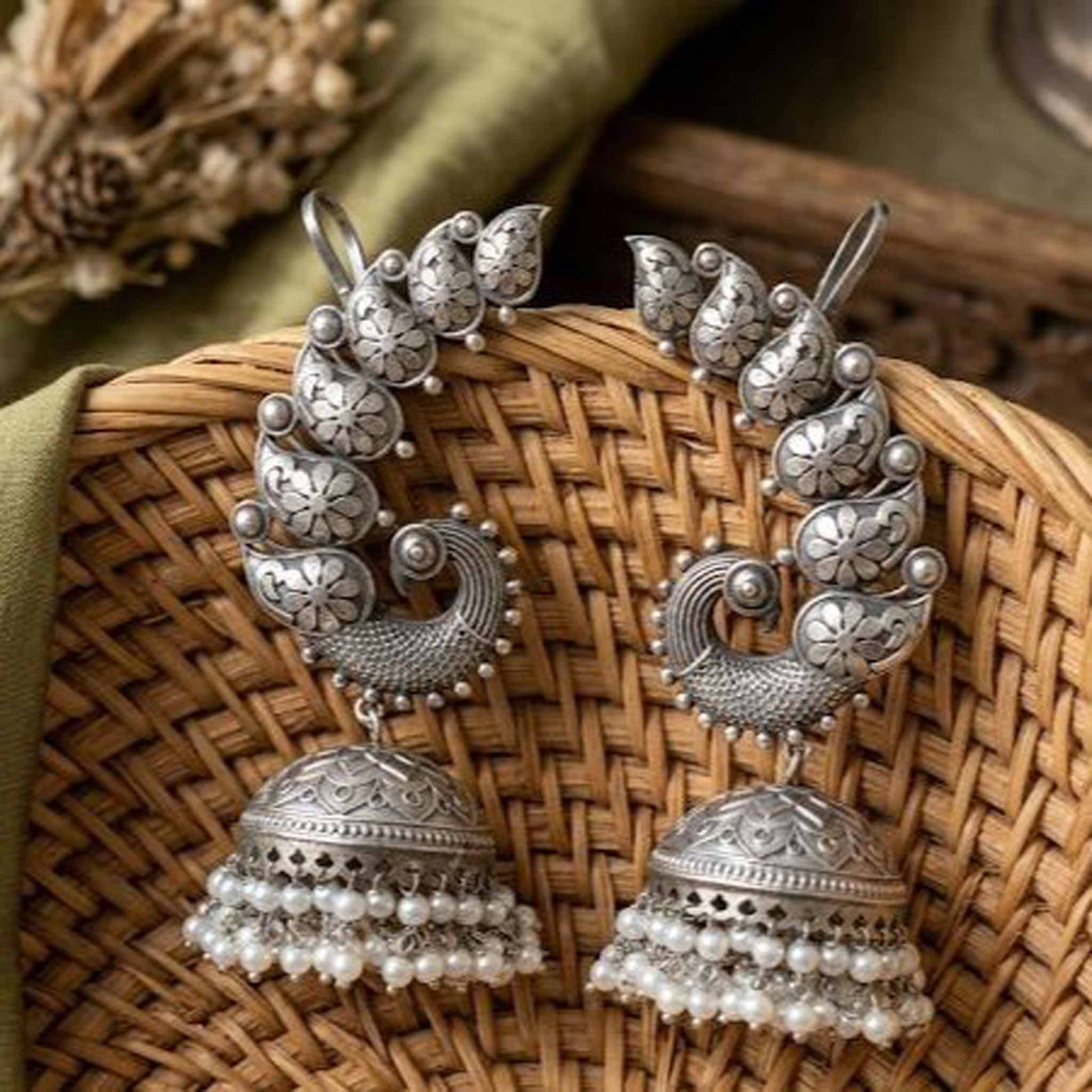 Peacock earcuff pearl jhumka earrings displayed on wicker basket