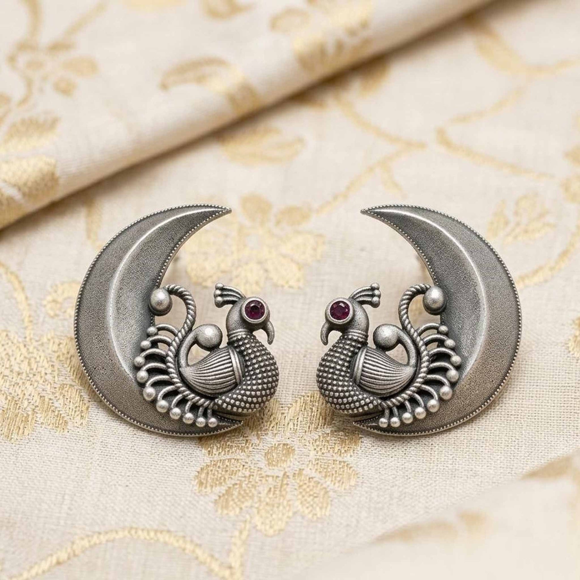 Peacock moon earrings placed on embroidered fabric backdrop